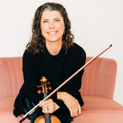 Sonja holding her violin sitting on a pink couch